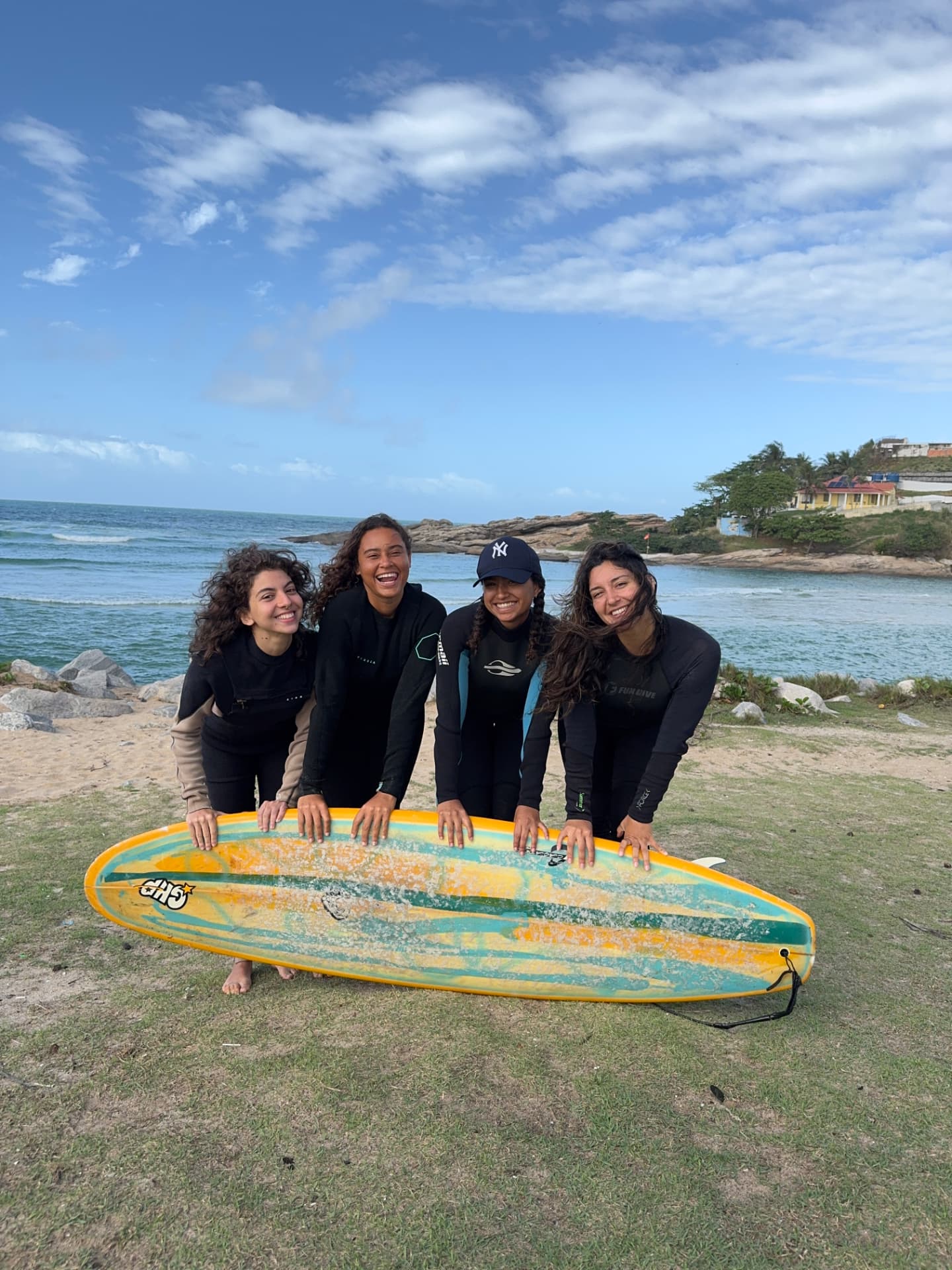 Quatro mulheres com uma prancha de surf à beira-mar